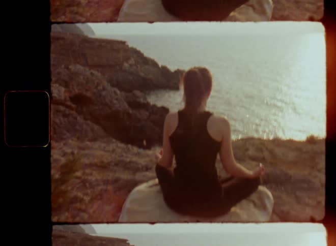 A meditating woman sitting in front of the ocean doing yoga in the sunset concentrating on her mind body connection and spiritual growth while deep breathing for a positive manifestation or affirmation as an earthing or grounding experience