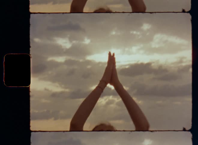 Woman doing yoga by the shore raising both arms before joining her hand above her head as she starts meditation by the sea connecting to the elements and wild nature surrounding her to find inner peace and stress relief while practicing self-care or love