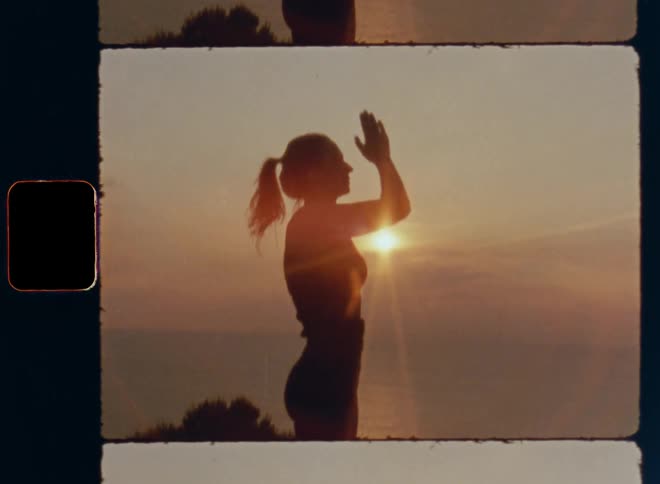 Attractive woman standing while doing yoga with ocean behind her and sunlight on the horizon raises her arms an joins hands high up in the air and places them in front of her heart to embrace the moment and find inner peace tranquility and solitude