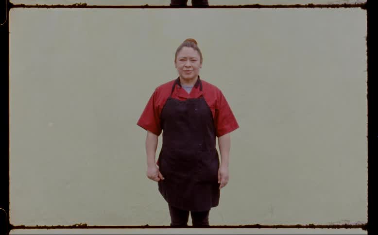 Woman standing and looking straight ahead wearing a black apron