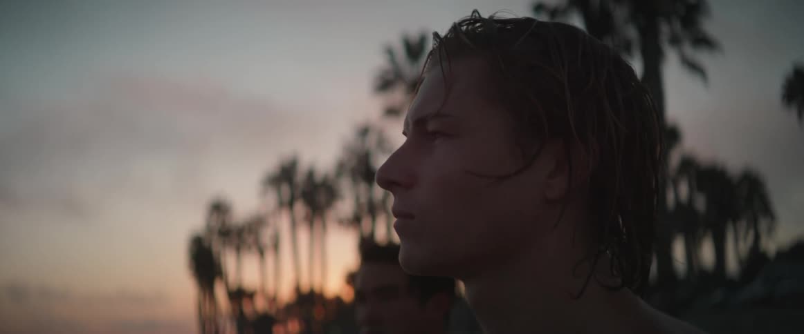 Two young men on a beach at dusk looking at the sea