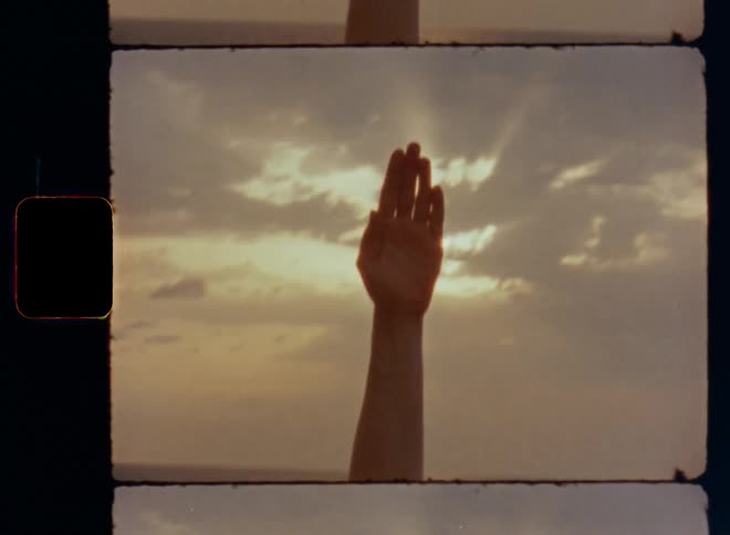 A young woman in light sports clothes raises her hand upwards towards the sun that shines through the clouds on a sunny yet overcast or gloomy summer day while working out and doing outdoor sports by the coast next to the water of the sea or ocean
