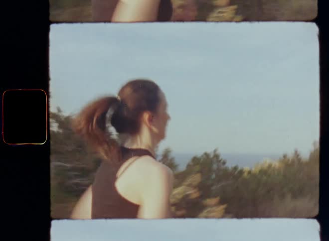 Persistent sportive woman wearing black tank top with brunette ponytail running with her back to the camera uphill towards the top of a mountain on a nature trail with the sea beside as symbol for power persistence perseverance endurance and motivation