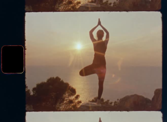 A standing woman is doing tree or mountain yoga pose during meditation session on high coastal cliff by the sea or Pacific Ocean with her silhouette and trees in front of the ocean and the brightly shining sun during sunrise or sunset on a warm summer day