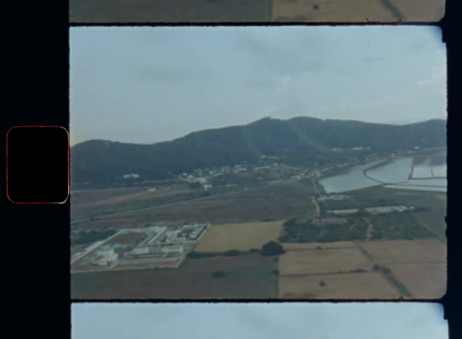 Aerial view of rural fields and water systems and mountains in the background on the horizon from a plane or aircraft that starts and is taking off to fly away from a rural area with small villages and houses surrounded by nature on Super-8 film