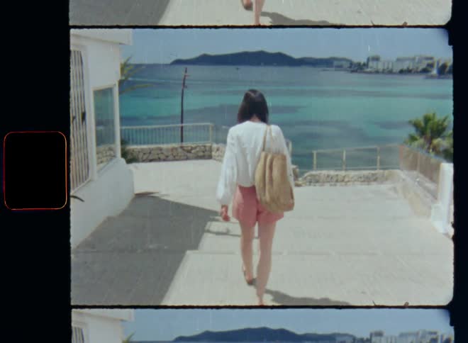 A woman with pink shorts and beige bag walks down the stairs on a promenade to enter paradise beach during summer vacation or a sightseeing trip in a holiday village or town by the coast with a beautiful bay and turquoise or aquamarine blue water