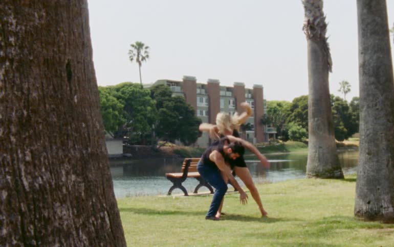 Man and woman dancing together in a park next to large trees on a sunny day