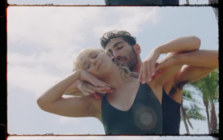 A man and woman dancing together outside on a sunny day near palm trees