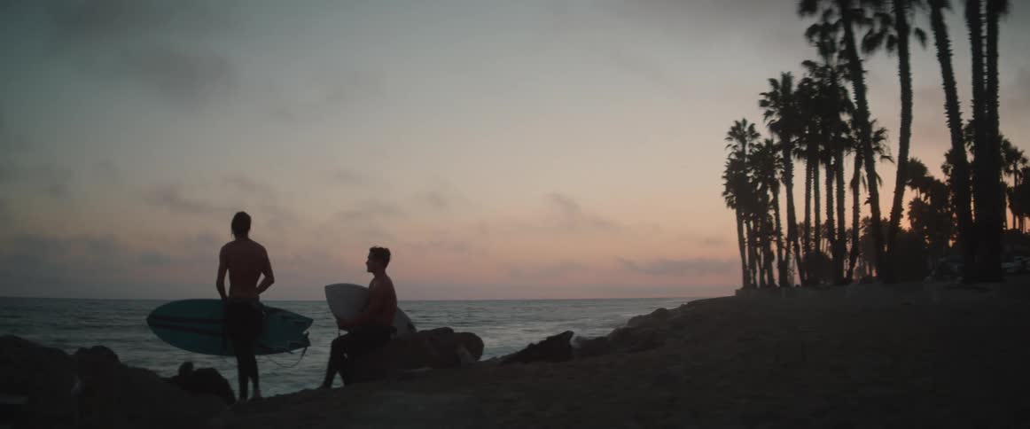 Two men are standing on the beach and holding surf boards