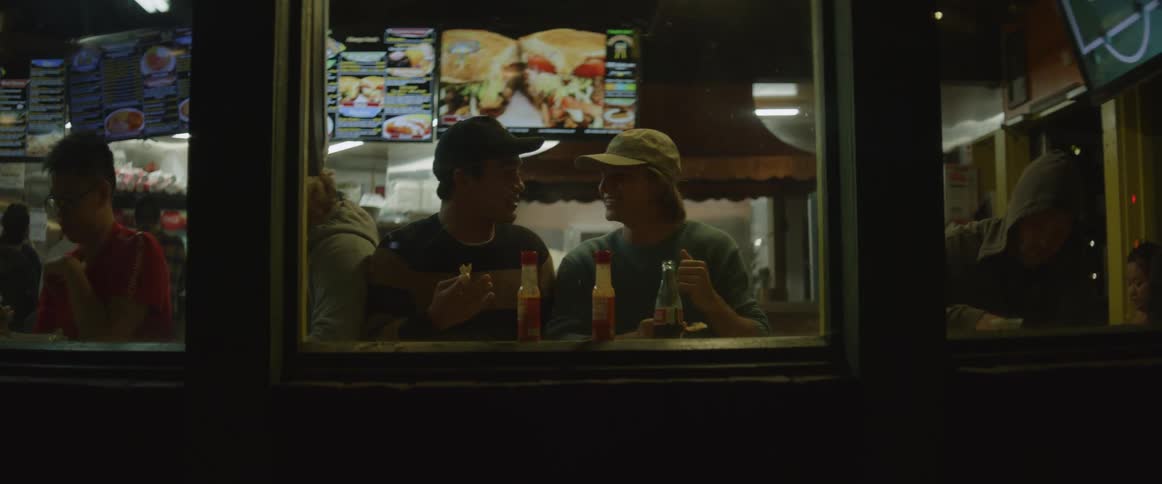 Two friends eating in a restaurant playfully push each other