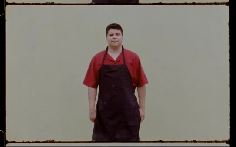 A man in an apron stands staring straight ahead