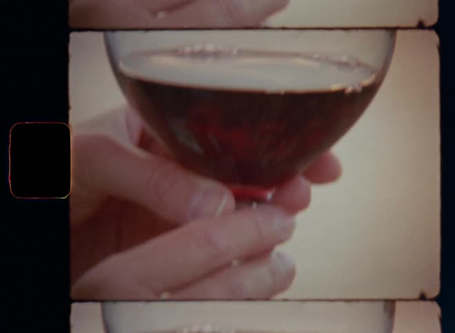 Old vintage close-up film footage of the hands of a woman holding a glass of red wine with a silver diamond ring in her finger celebrating the engagement with a toast and drinking alcohol on a warm spring evening during their anniversary vacation