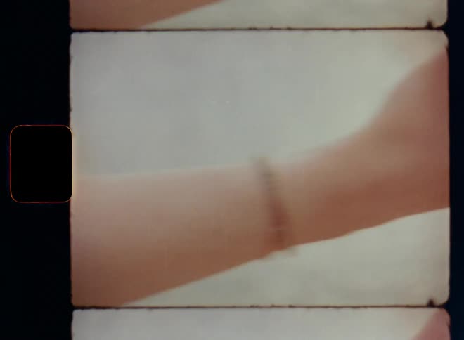 Dynamic handheld Super 8mm film footage of the trained and muscular arm of a brunette woman that is smiling while doing yoga or meditating next to the sea as he forms a meditation mudra or chakra with her hand and fingers with a blurry background