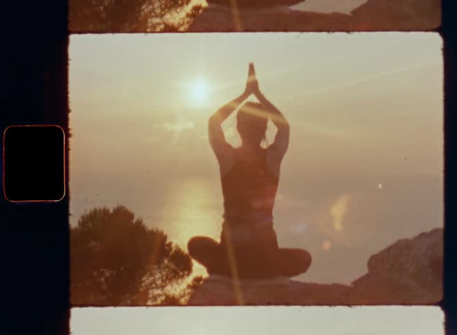 A fit and healthy woman is doing yoga on the mountain overlooking the Indian Ocean with great view as the sun rises and she raises her arms and joins them above her body connected to her mind as the bright sunshine flares and glares
