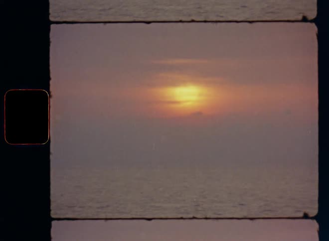 The sun is obscured or covered by a layer of hazy clouds as a large seagull bird flies over the open ocean during sun set with great view of the wide horizon above the water surface of the sea with waves and high tides on Super-8 film