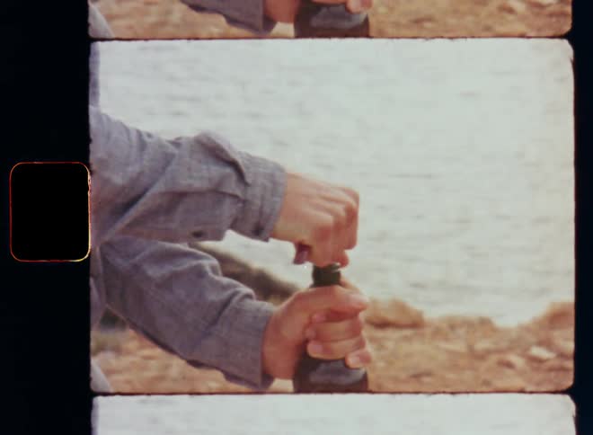 Unrecognizable person wearing a gray shirt with long sleeves is opening a green red wine glass bottle with a bottle opener to remove the cork at the beach or on a cliff by the ocean during sun set on a warm summer vacation day celebrating the holidays