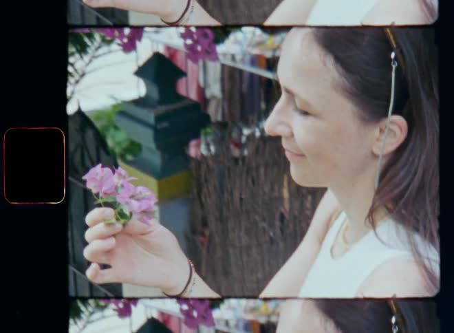 Dynamic handheld 8mm film of a brunette woman with sunglasses on her head picking a purple or pink flower from a tree and smelling it before she starts smiling with closed eyes inspired by the fresh smell and scent of mother nature during spring time
