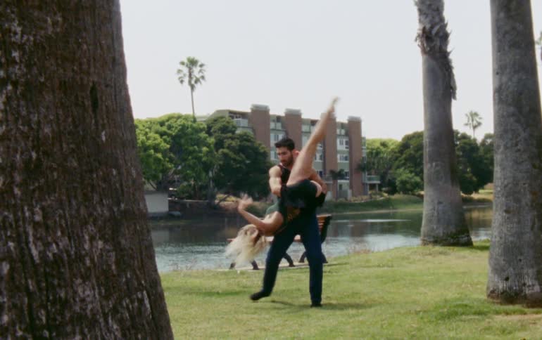 A man and woman perform a dance next to a lake