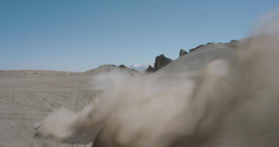 A person performing a motocross maneuver sending sand and dust flying in an outdoor environment