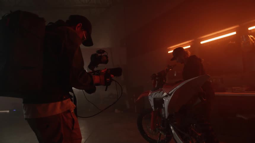 Film maker in a dim lit room shooting a movie with a woman holding a motocycle