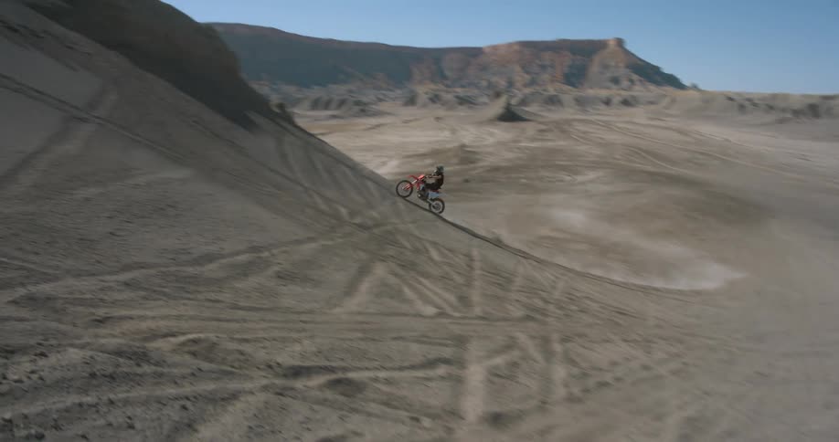 Aerial of a motorcycle climbing a sand dune in the desert up and down