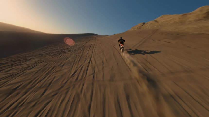 Aerial of a person in a motorcycle speeding up and jumping off a desert dune