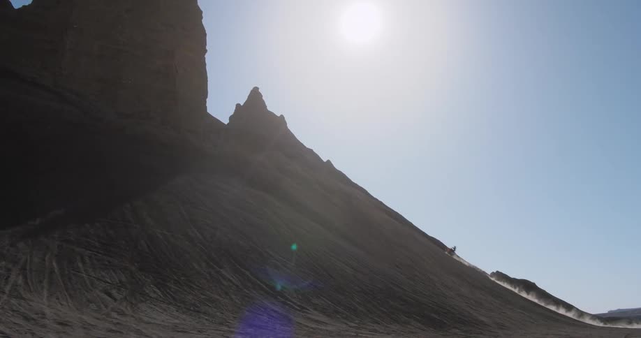 A motorcyclist rides up and down a sandy mountain slope in a desert