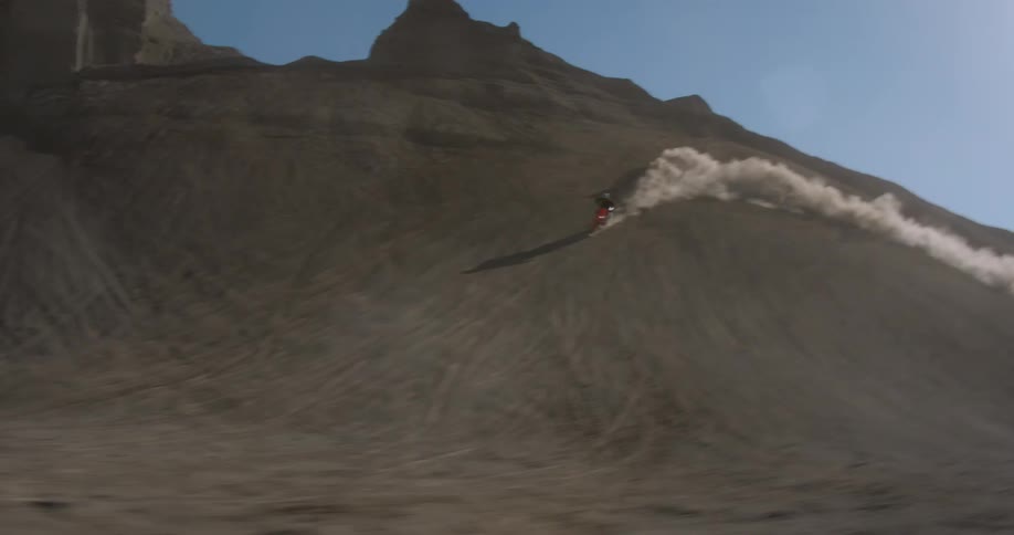 A person riding a mountain bike doing a stunt up and down the hill causing dust to fly around