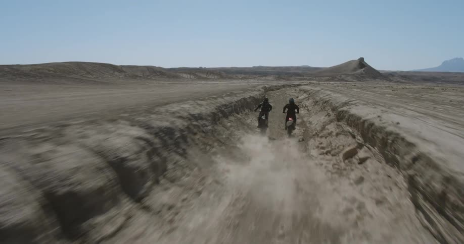 Two people doing motocross in a hole in a desert region