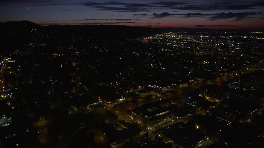 Aerial view of Downtown Portland at night approaching Interstate 405 with illuminated buildings light traffic and a reddish sky in the background