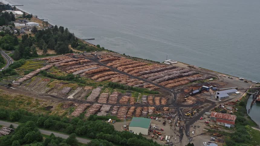 Aerial footage of a lumber yard filled with piles of lumber along the Columbia River in Warrenton Oregon on an overcast day