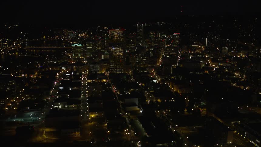 Nighttime aerial footage of US Bancorp Tower in downtown Portland Oregon with trains passing by Union Station and a partly cloudy sky