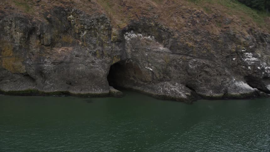 Aerial footage tracks a cave at the base of a cliff in Cape Disappointment Washington on a cloudy day