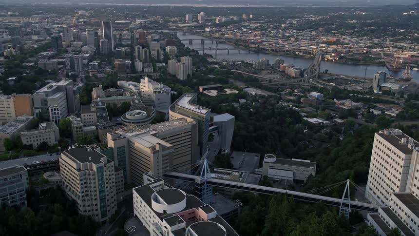Aerial footage of Oregon Health and Science University orbiting over Downtown Portland Oregon during sunset revealing the city's high-rise buildings the Willamette River and the vibrant atmosphere of the bustling metropolis