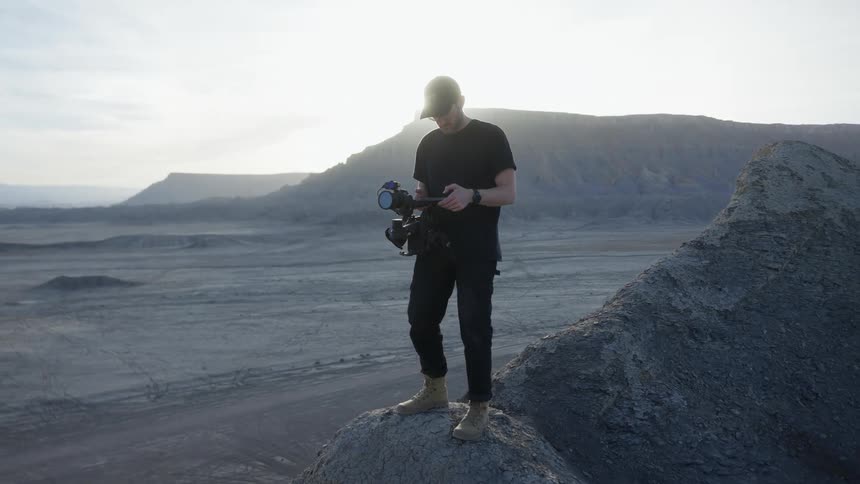 A filmmaker looks down at a camera in a desert at dawn