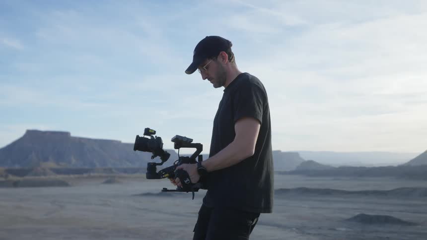 A man handling and filming with a professional camera in an outdoor environment with mountains