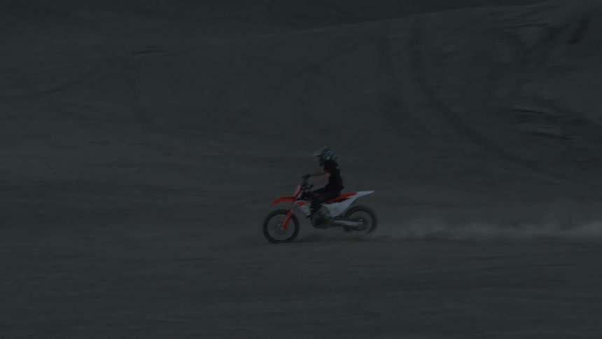 A man does a large jump over a sand dune on a dirt bike