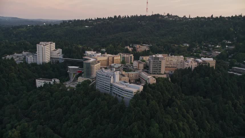 Aerial footage at twilight of Oregon Health and Science University in Portland Oregon flying away from the buildings in a partly cloudy sky
