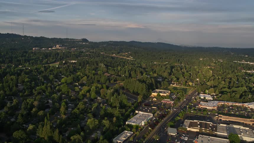 Approaching and flying over suburban homes and a shopping center at sunset in Beaverton Oregon with partly cloudy skies in the background