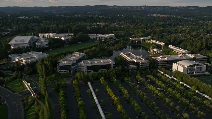 Aerial footage at sunset of Nike Headquarters in Beaverton Oregon with a view of the modern complex building and surrounding office buildings during a partly cloudy evening in the Pacific Northwest