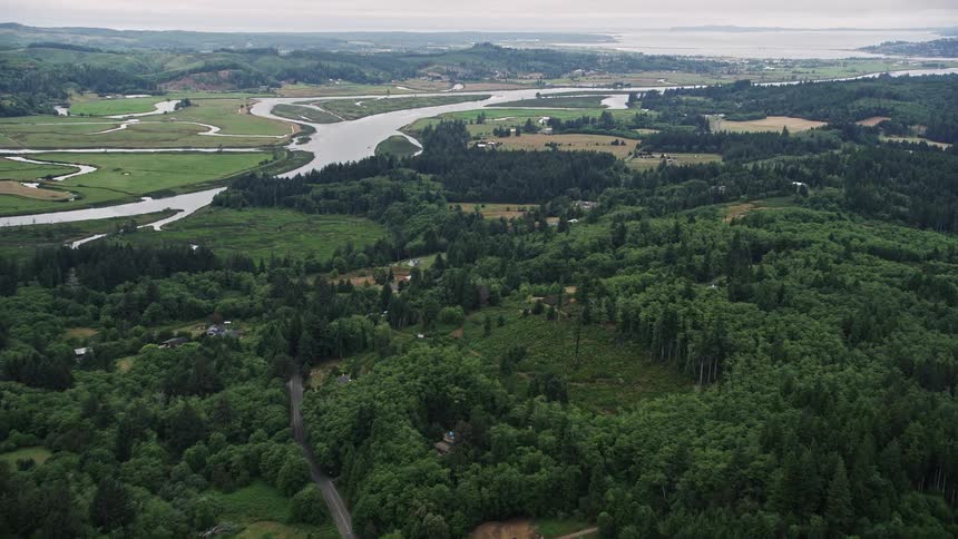 Approaching rural homes alongside the Youngs River in Astoria Oregon with ranch fields on one side showcasing the rustic and agricultural charm of the Pacific Northwest during a sunny summer day