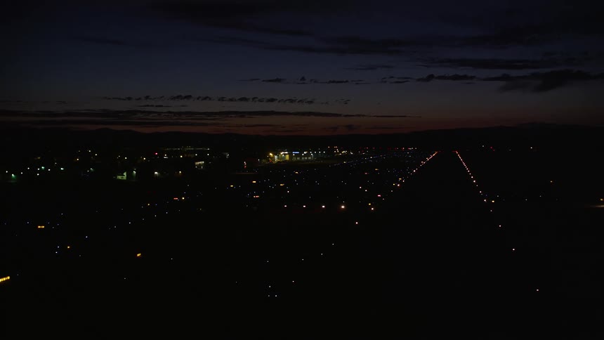 An aerial view of an airplane landing at Hillsboro Airport in Oregon at night showcasing the partly cloudy skies and the busy airfield