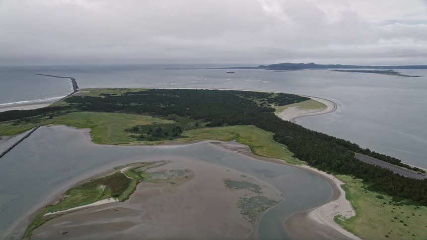 Aerial footage of an overcast day approaching Clatsop Spit in Oregon by the Columbia River showcasing the shoreline and nature