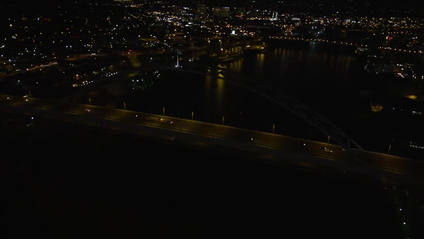 Aerial footage of Fremont Bridge orbiting to reveal Downtown Portland Oregon at night with high rise buildings light traffic and partly cloudy skies