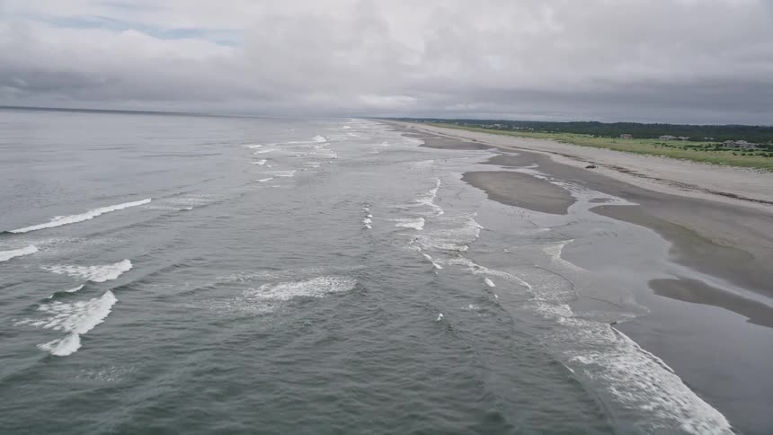 Aerial view of ocean waves rolling in near a beachgoer on a cloudy day in Seaview Washington during summer