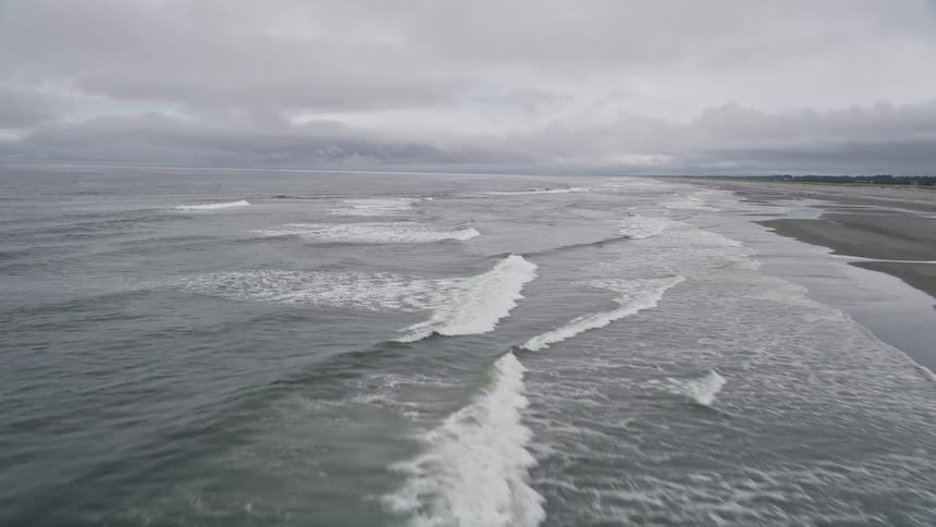 Aerial footage of crashing ocean waves approaching an empty beach in Seaview Washington on a cloudy summer day