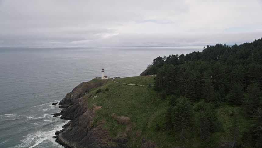 Aerial footage of flying away from North Head Light on a coastal cliff showcasing the scenic shoreline of Ilwaco Washington during the day