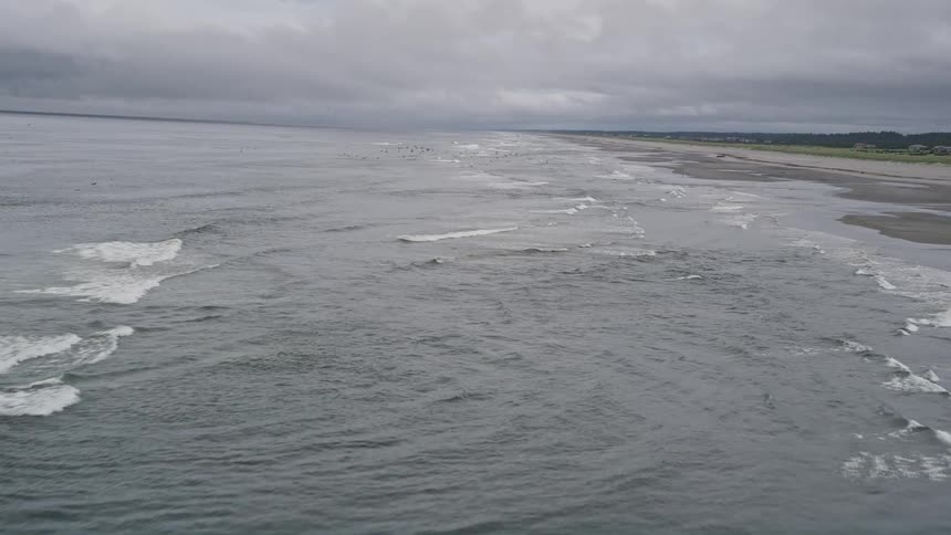 Aerial footage captures crashing waves on a populated beach in Seaview Washington as a lone beachgoer enjoys the scenic coastal views