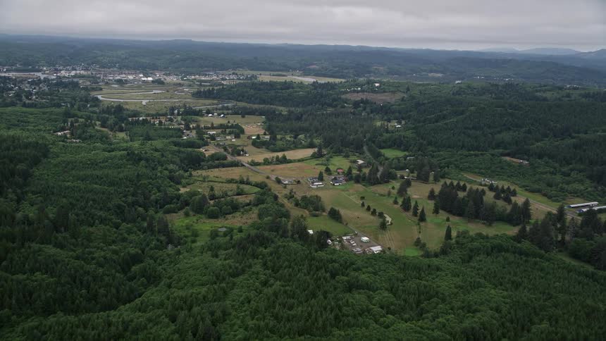 Aerial view of small farms in Raymond Washington as the camera approaches from the nearby forest showcasing the rustic and agricultural landscape of the Pacific Northwest during the summer