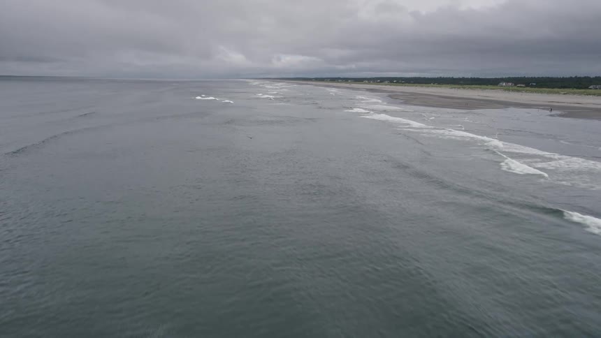 Aerial view of ocean waves rolling towards a Long Beach Washington shoreline with people enjoying the beach during a sunny summer day